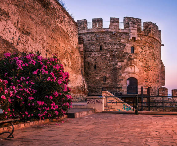 Ancient tower and stone walls with blooming flowers at sunset in Thessaloniki, Greece