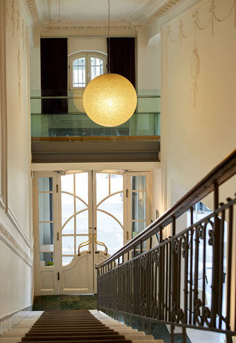 Elegant entrance hall with ornate white doors, decorative molding, a classic wrought-iron staircase railing, and a large glowing globe pendant light creating a welcoming atmosphere