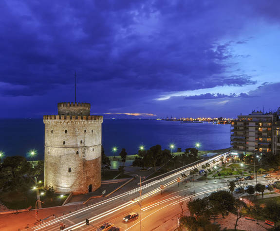 White Tower illuminated on Thessaloniki waterfront with city lights and dramatic evening sky, Greece