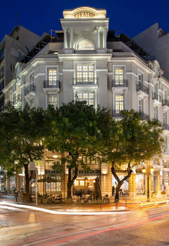Striking nighttime view of The Excelsior Hotel, with its beautifully lit neoclassical façade, ornate balconies, and vibrant street-level café terrace, set on a lively corner in the heart of the city